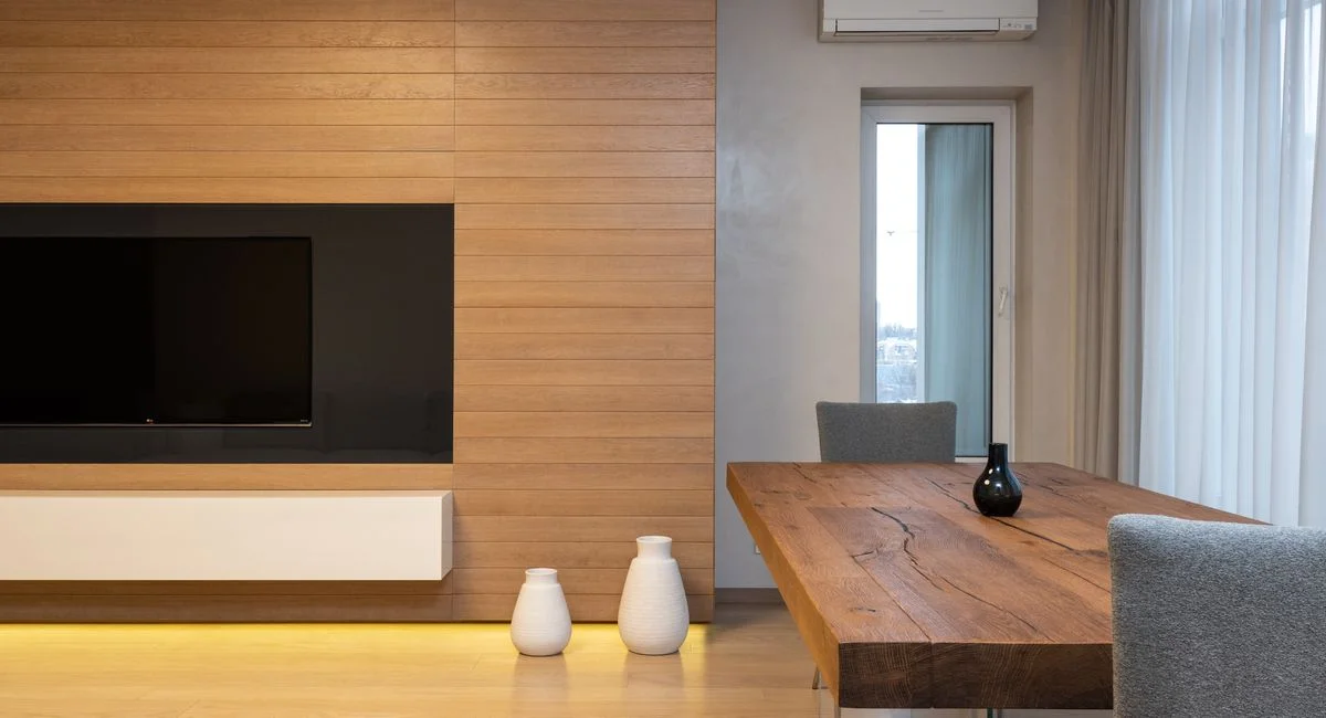 Modern TV set on wooden wall in spacious living room with table and decorated with lights and ceramic vases