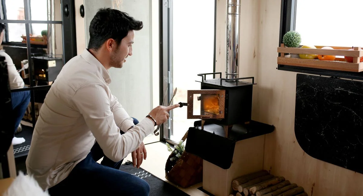 A man lights a wood stove inside a cozy room, creating a warm and inviting atmosphere.