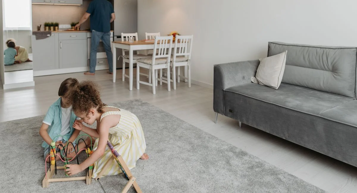 Two children playing on a rug as their father cooks in a modern, cozy home setting.