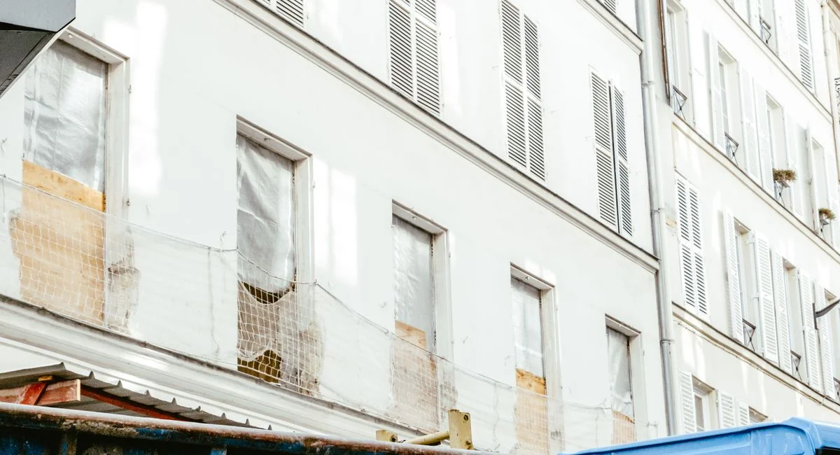 Exterior view of an unfinished urban building with covered windows and construction materials.