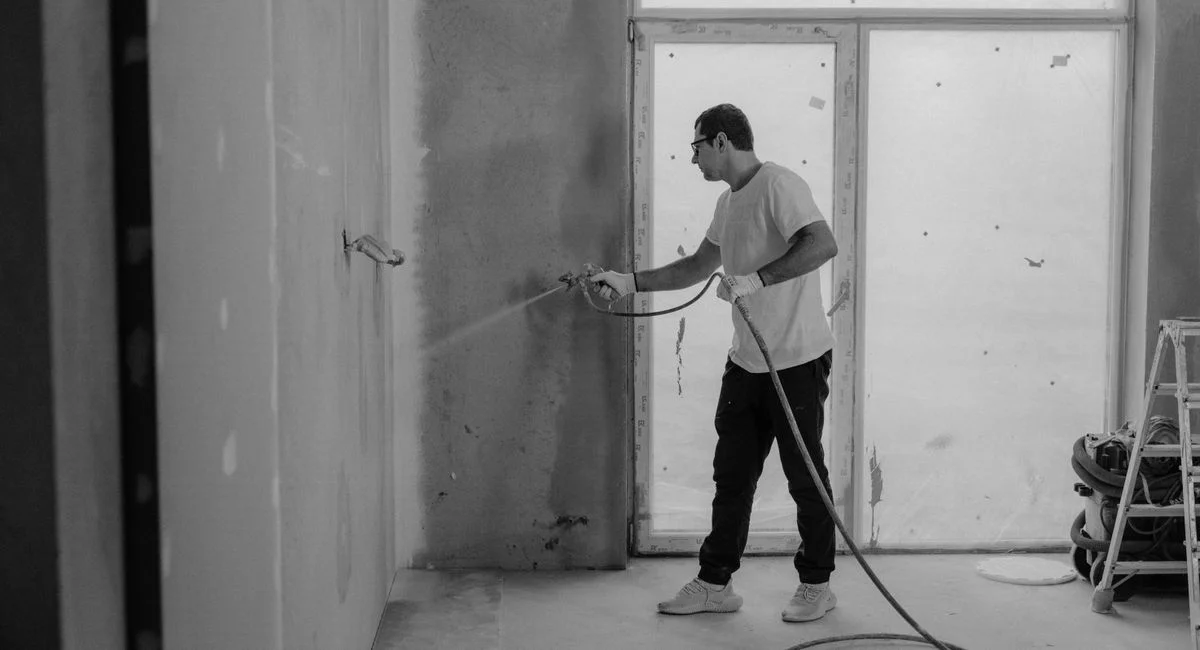 A worker paints an interior wall with a spray gun during a renovation project.