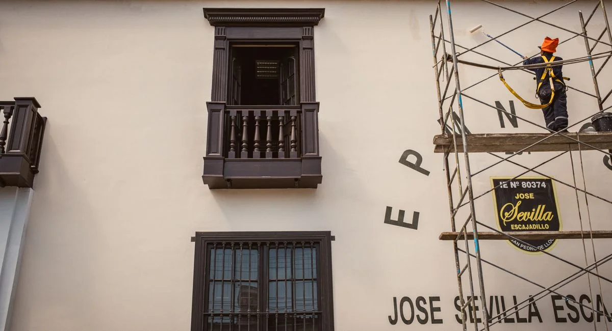 A construction worker paints a building facade while standing on scaffolding, showcasing architectural restoration.