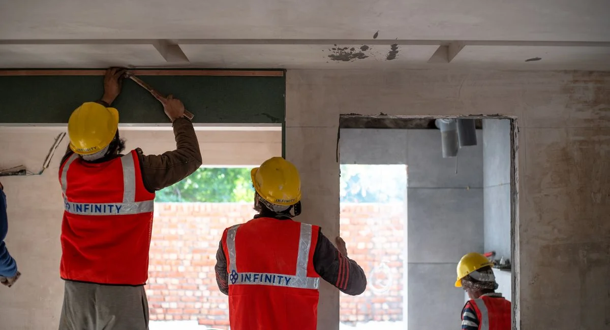 Construction workers renovating interior space in Delhi with safety gear and tools.