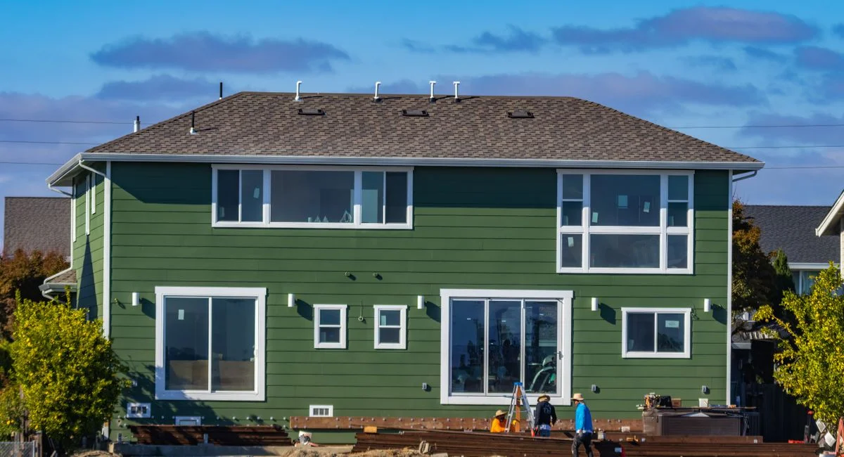 A modern green house under construction with blue skies and workers outside.