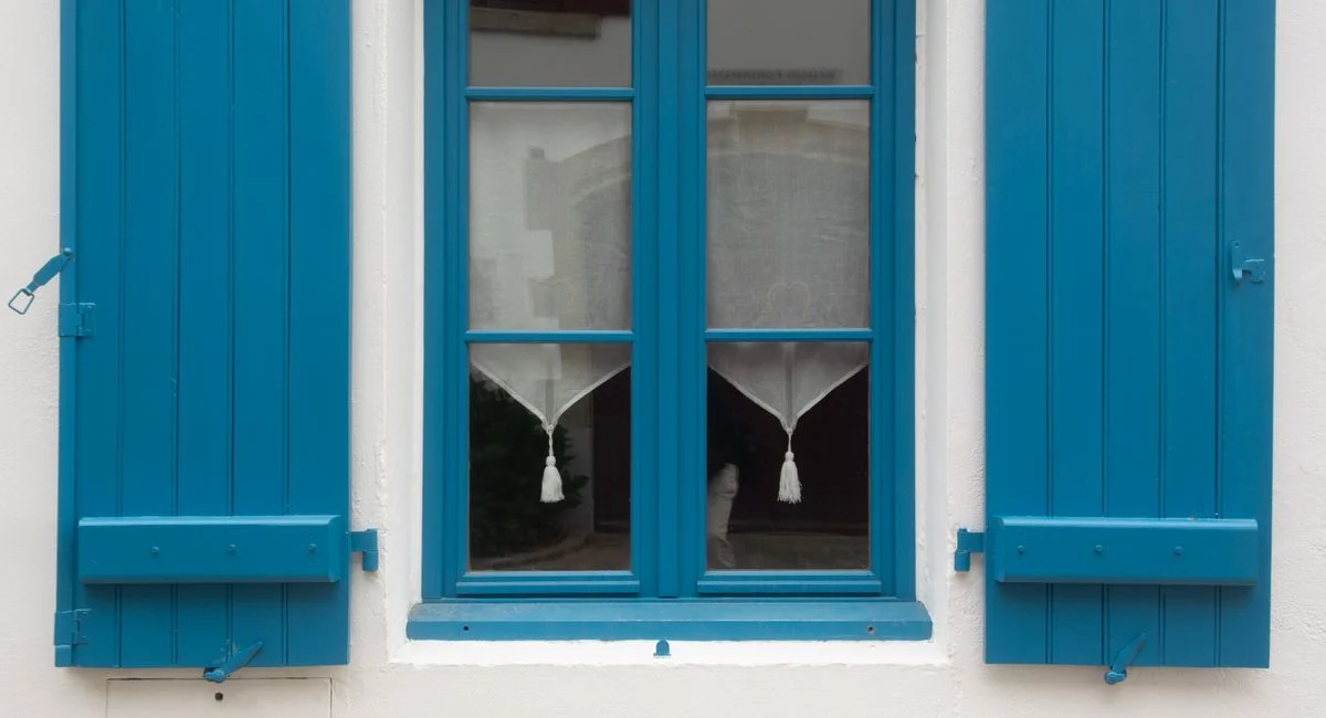 Close-up of blue shutters and window on a rustic white wall, showcasing classic architecture.