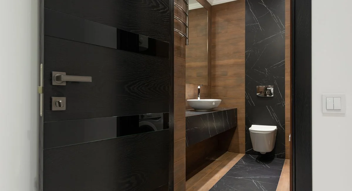 Sleek bathroom with black marble tiles and wooden accents, featuring a modern sink and toilet.