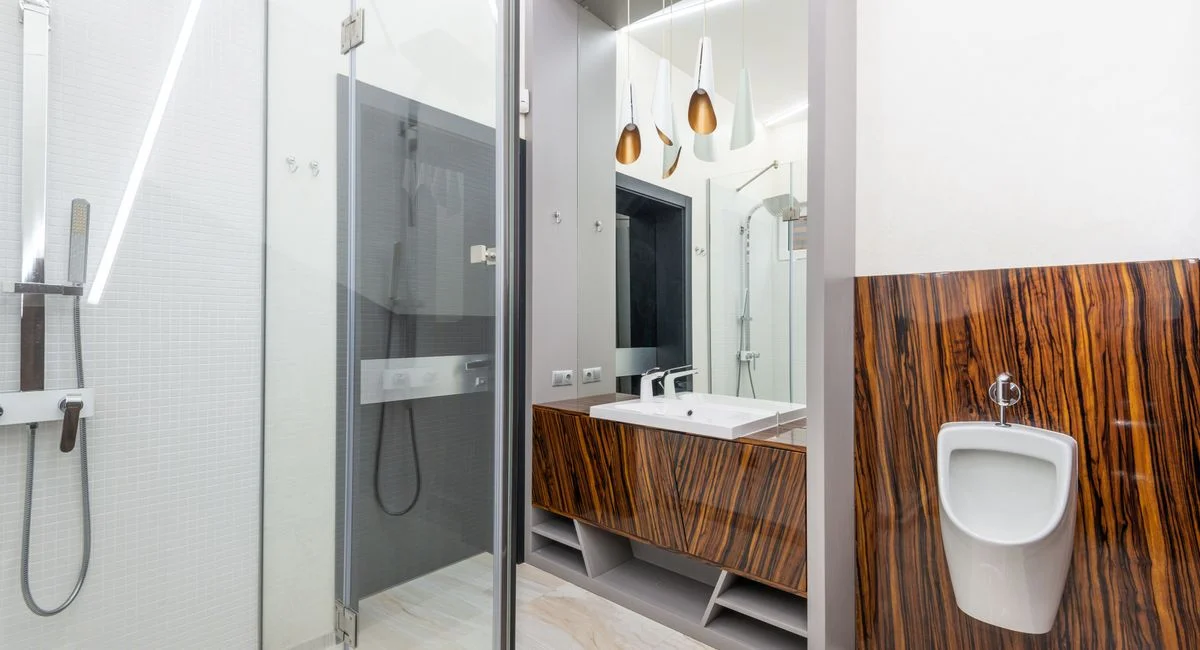 Interior of contemporary bathroom with glass shower cabin and ceramic sink and urinal
