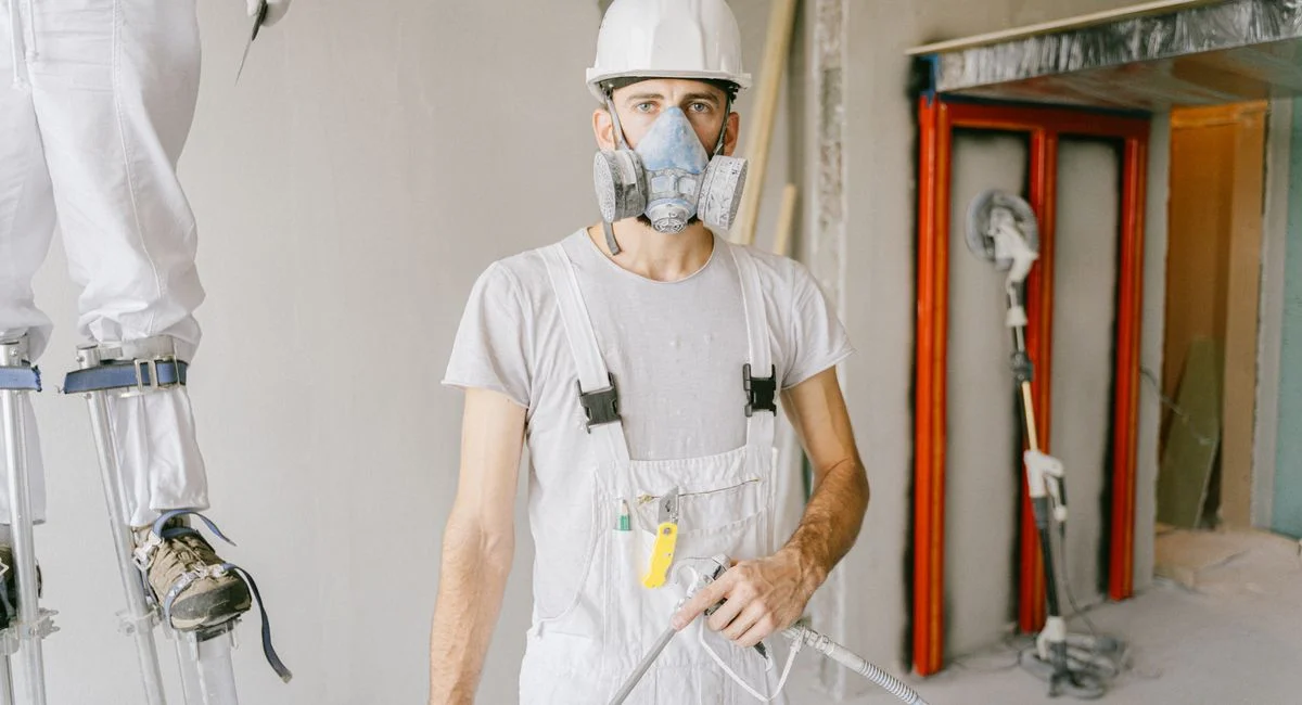 A construction worker wearing protective gear and prepping the wall during renovation indoors.