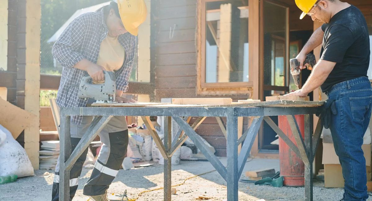 Two construction workers using power tools on a sunny day.