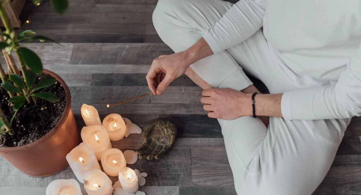 Person meditating indoors with candles and incense. A calm and peaceful setting for relaxation.