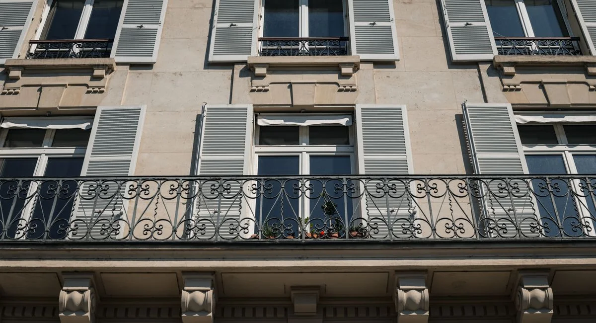 Elegant Parisian apartment facade with ornamental iron balcony and shutters in the city of Paris.