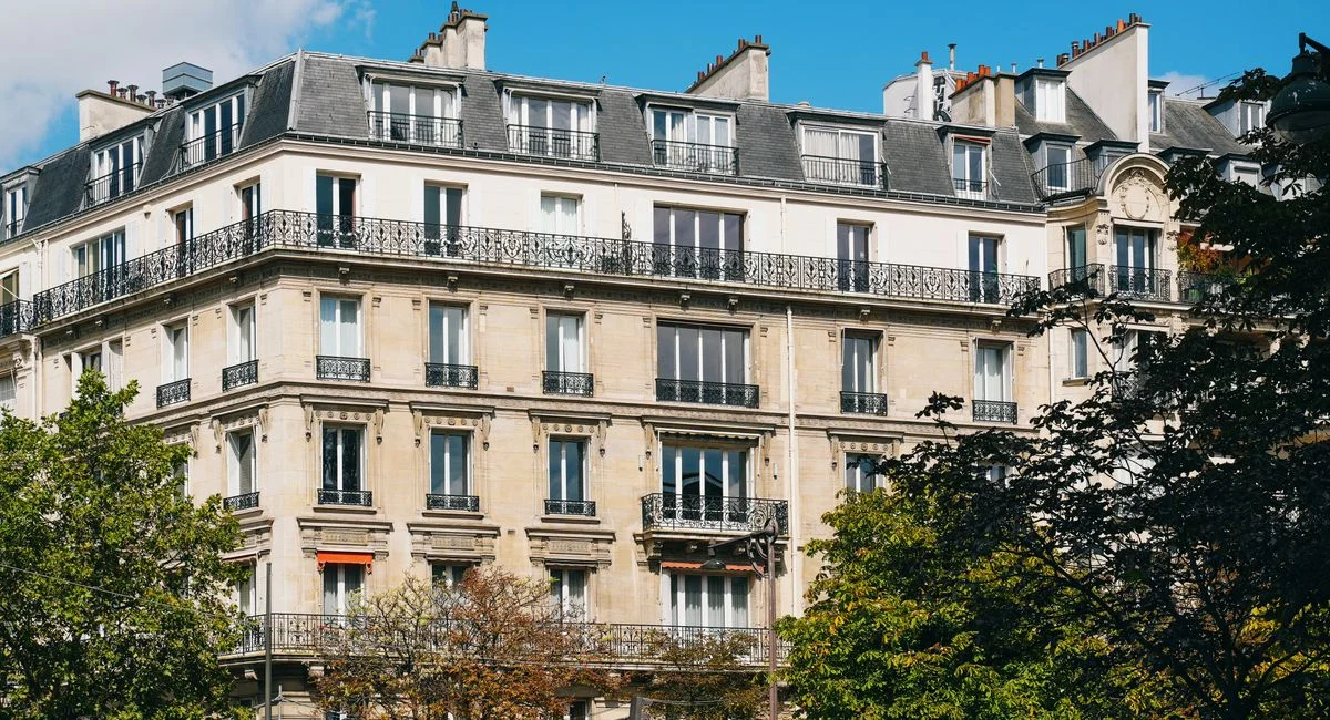 Elegant French architecture with trees under a bright sky, showcasing Parisian charm.