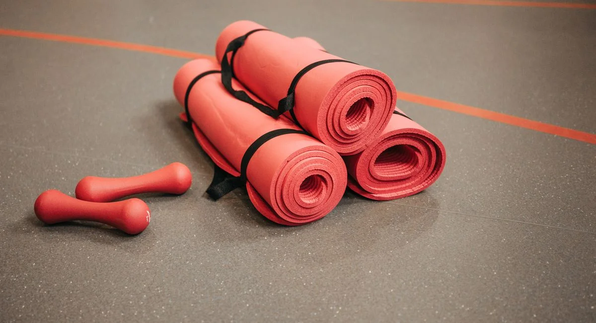 Red exercise mats and dumbbells on a gym floor, perfect for home or studio fitness.