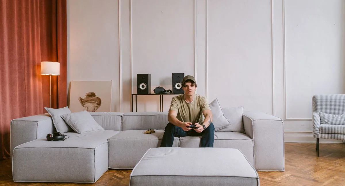 A young man sits on a modern sofa playing video games in a stylish living room interior.