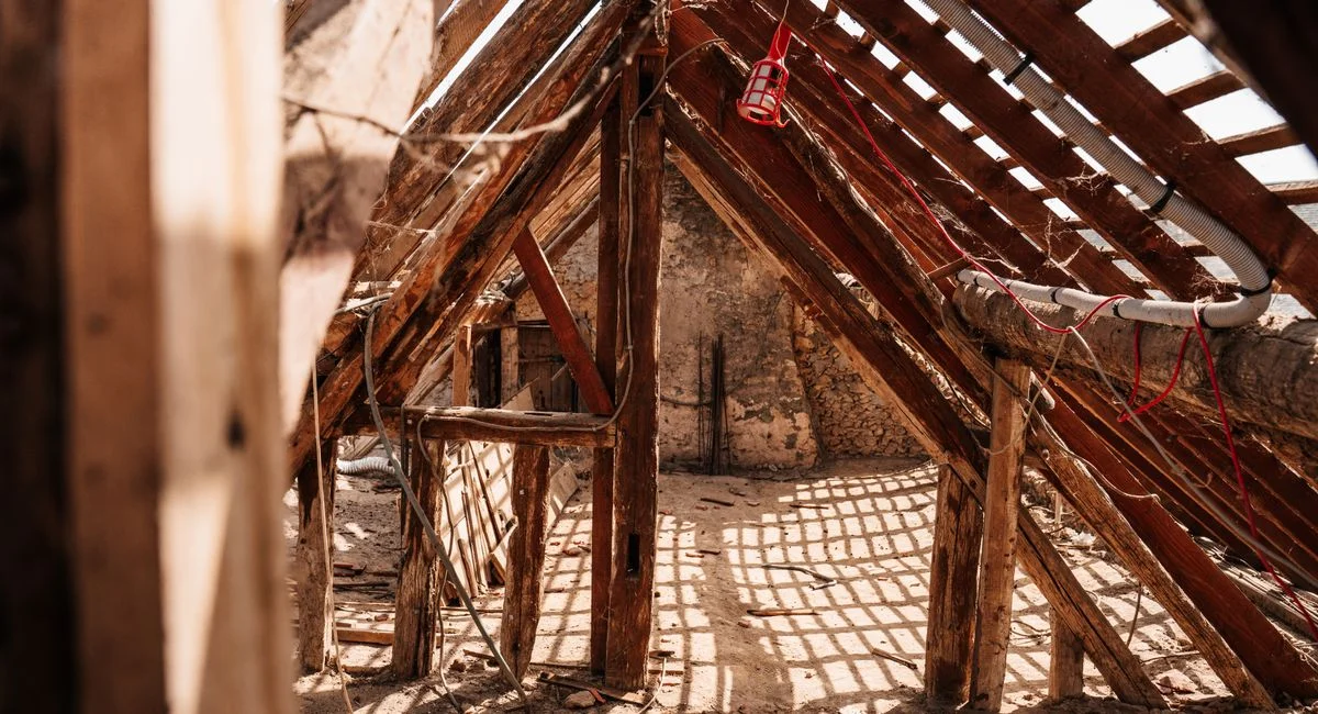Interior view of wooden framing and rafters in a partially constructed attic space, highlighting a rustic and textured struct