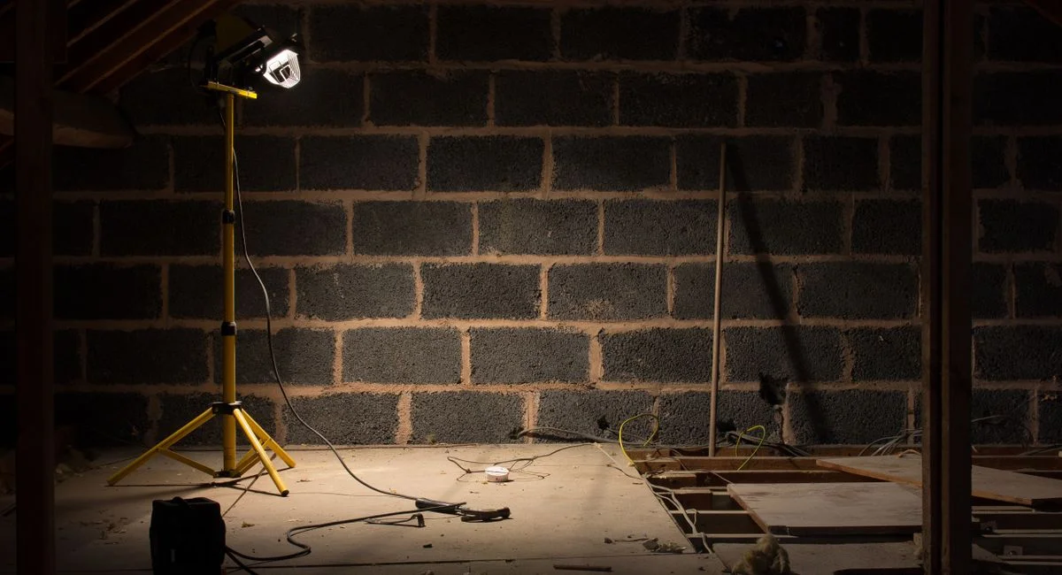 A dimly lit attic space under renovation with a construction lamp illuminating the scene.