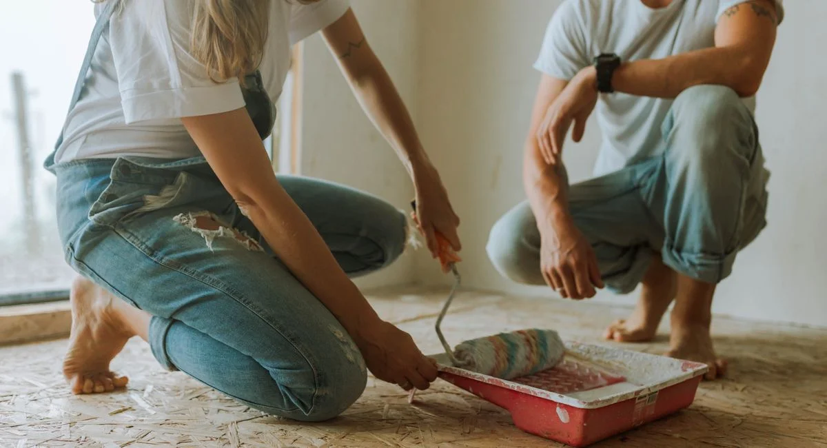 Young couple painting a room. They are kneeling on the floor, involved in a home renovation project.