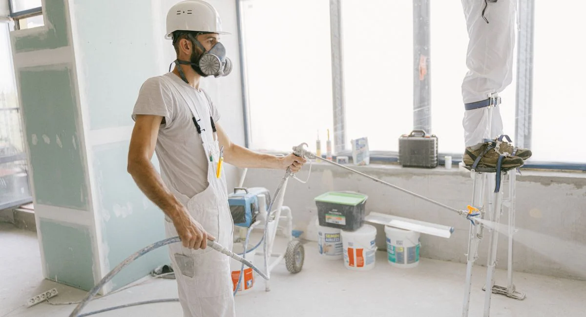 Two construction workers wearing protective gear and painting interior walls for a renovation project.