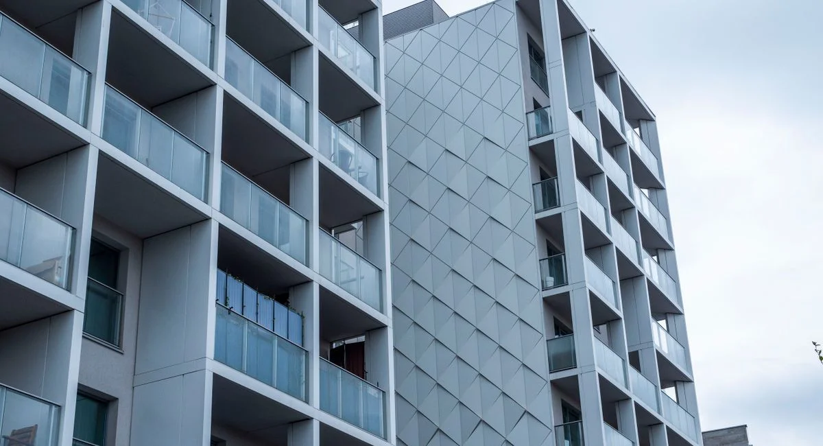 Contemporary glass facade of a city apartment building under a cloudy sky.