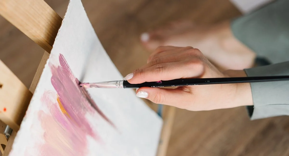 Artist's hand painting with brush on canvas, capturing creativity and artistry.