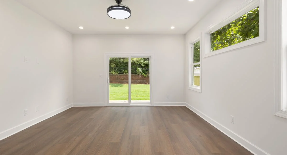 Bright empty room with wooden flooring and sliding glass doors leading to a garden.