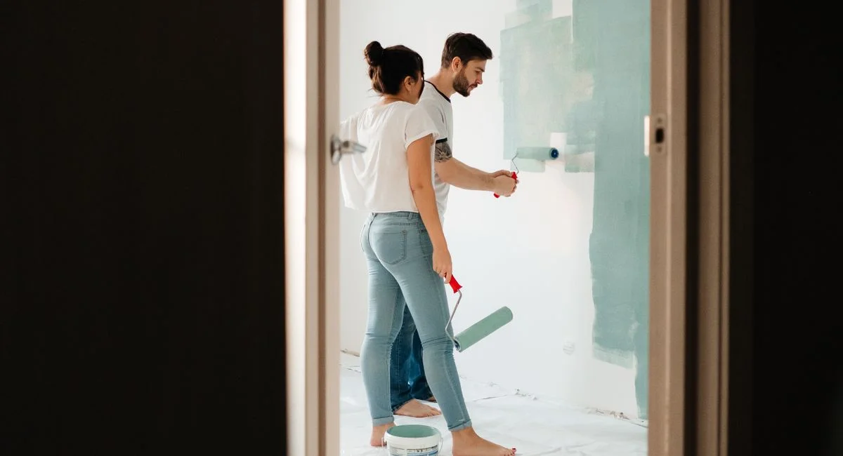 A man and woman painting a room wall with rollers, showcasing teamwork in home renovation projects.