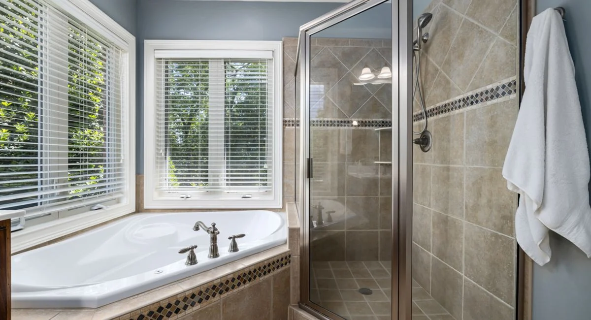 Elegant bathroom with glass shower, soaking tub, and large windows offering natural light.