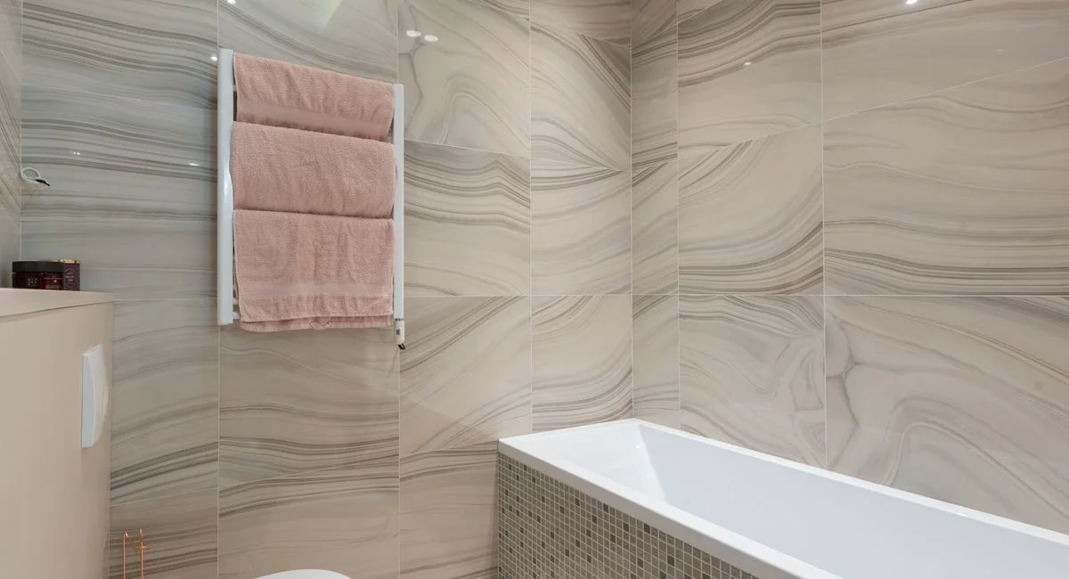 Contemporary bathroom interior with toilet bowl against bathtub and tiled walls with towels on rack in light house