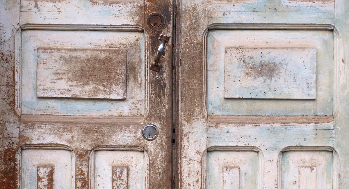 Close-up of rustic vintage wooden double doors with antique hardware and textured finish.