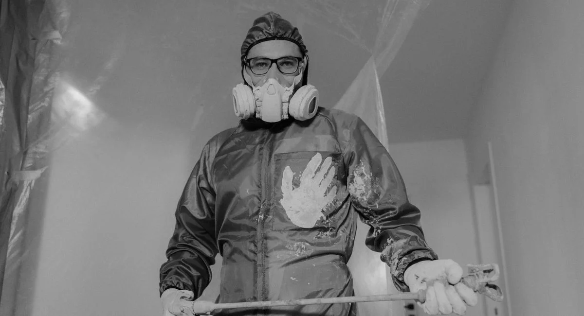 A worker in protective gear painting indoors during a home renovation project.