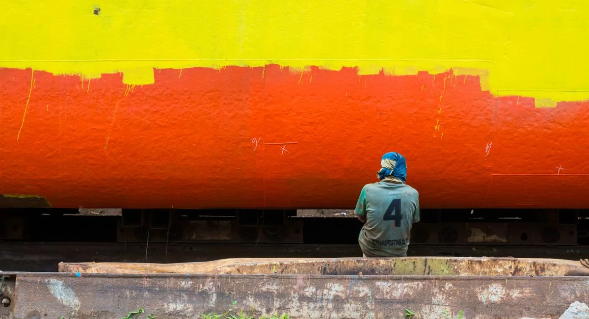 A shipyard worker painting a boat in vibrant colors in Dhaka, Bangladesh.