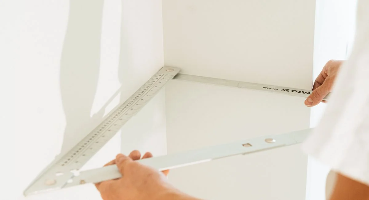 Close-up of a person measuring a corner with a metal square for home improvement or carpentry.