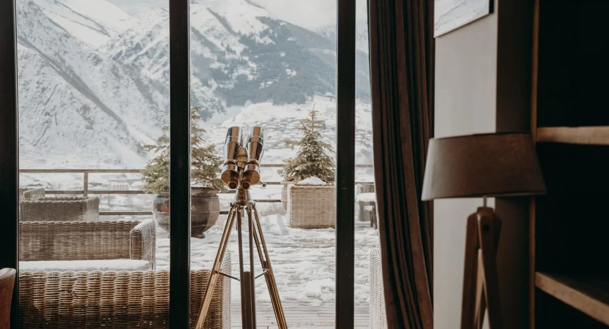 A cozy room with a telescope facing snow-covered mountains through large windows.