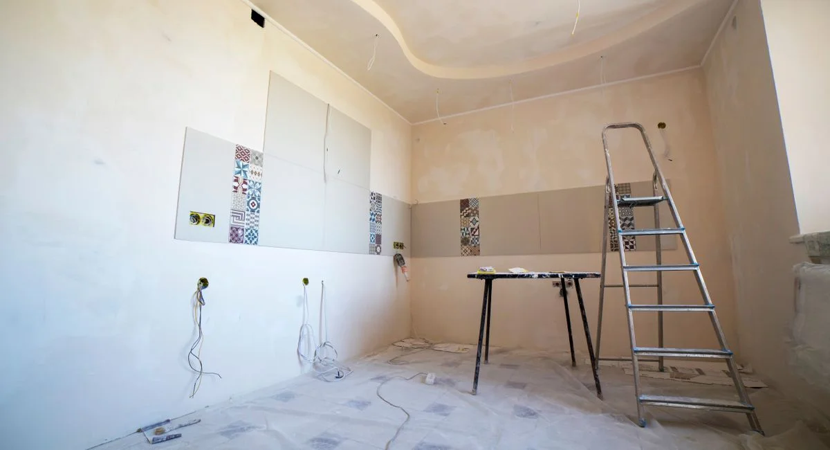 Interior view of a room under renovation with paint, tiles, and tools.