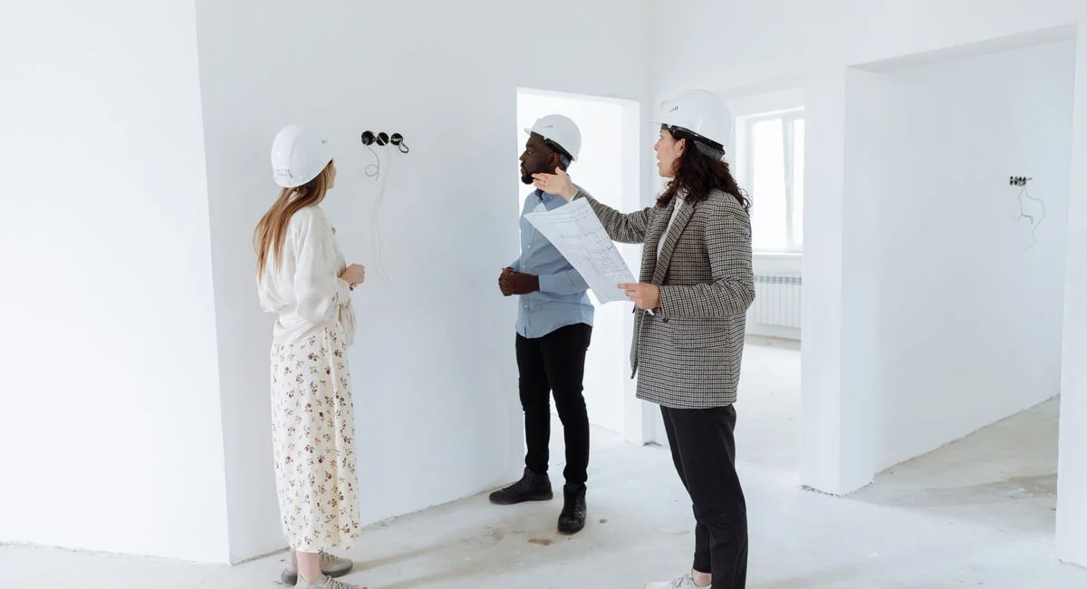 Three professionals discuss design plans inside a new house wearing hard hats.